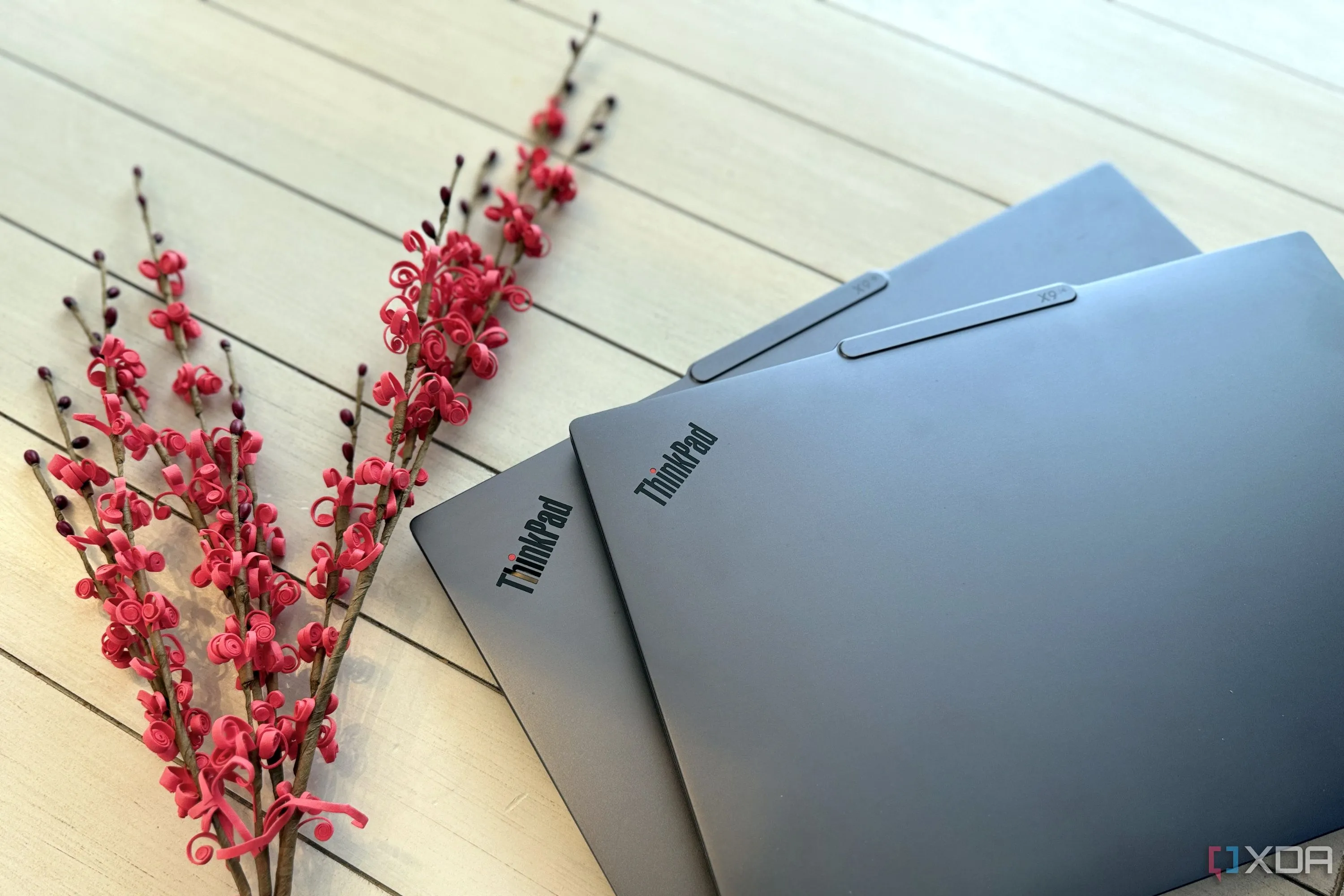 Hai mẫu laptop Lenovo ThinkPad X9 Aura Edition 14 inch và 15 inch đặt phẳng cạnh một cành hoa đỏ, thể hiện sự mỏng nhẹ
