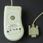 Hình ảnh chuột bi kết nối qua cổng nối tiếp (serial port) hoặc PS/2, minh họa thiết kế cũ và con lăn ở mặt dưới.