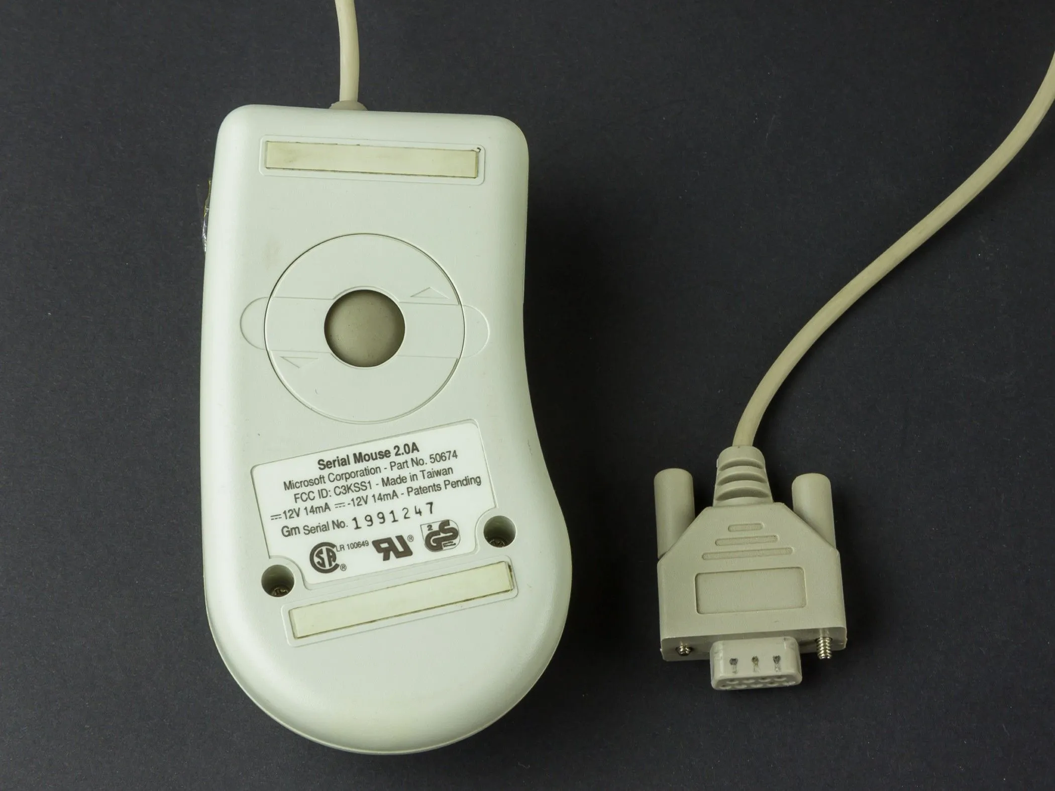 Hình ảnh chuột bi kết nối qua cổng nối tiếp (serial port) hoặc PS/2, minh họa thiết kế cũ và con lăn ở mặt dưới.