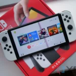 Hình ảnh máy chơi game Nintendo Switch OLED màu trắng với joy-con trên dock, minh họa phần cứng cũ của Switch đời đầu