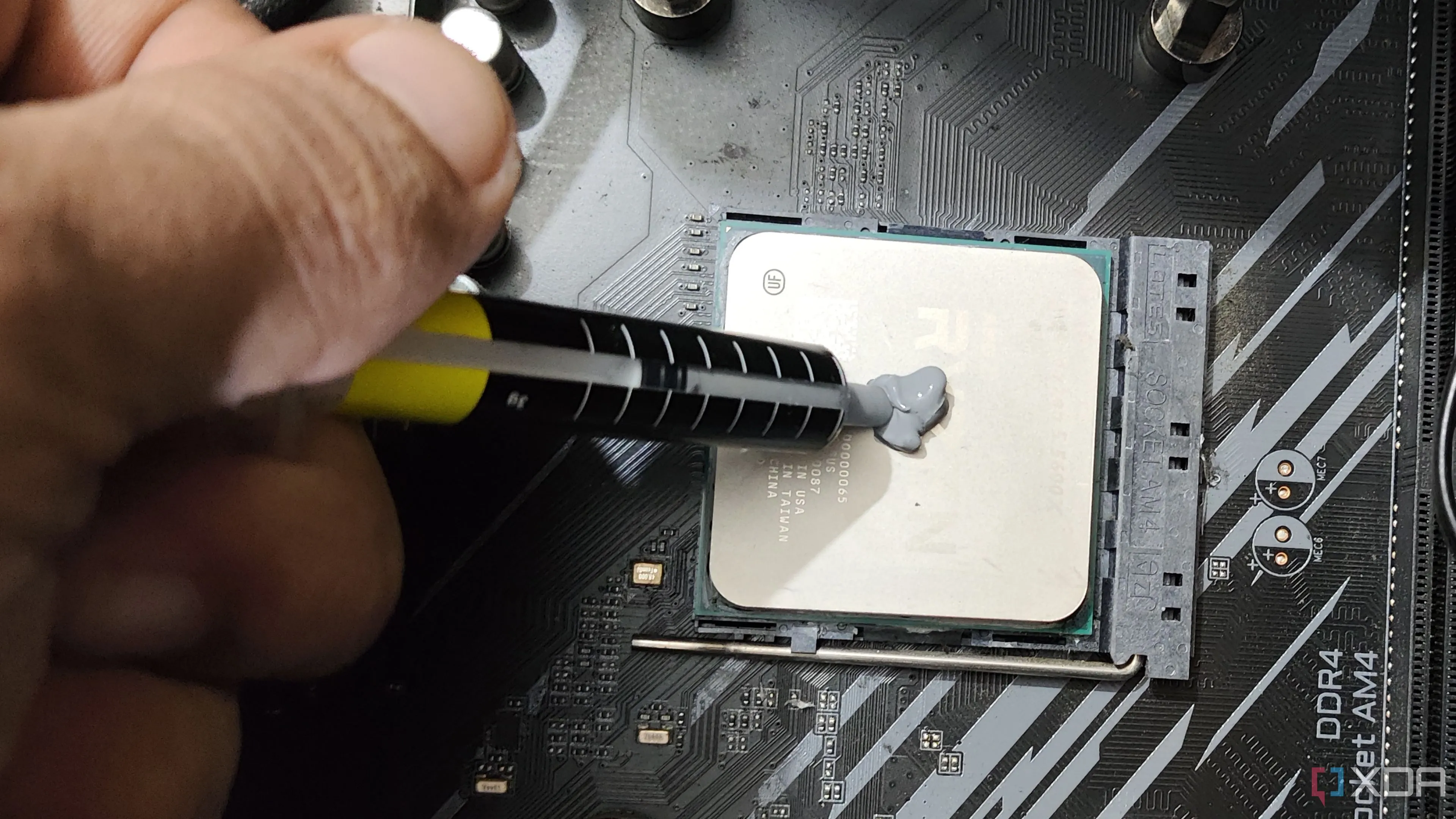 Hình ảnh một người đang bôi keo tản nhiệt lên chip Ryzen 5 5600X, minh họa quy trình thay keo tản nhiệt để cải thiện khả năng làm mát CPU/GPU laptop.