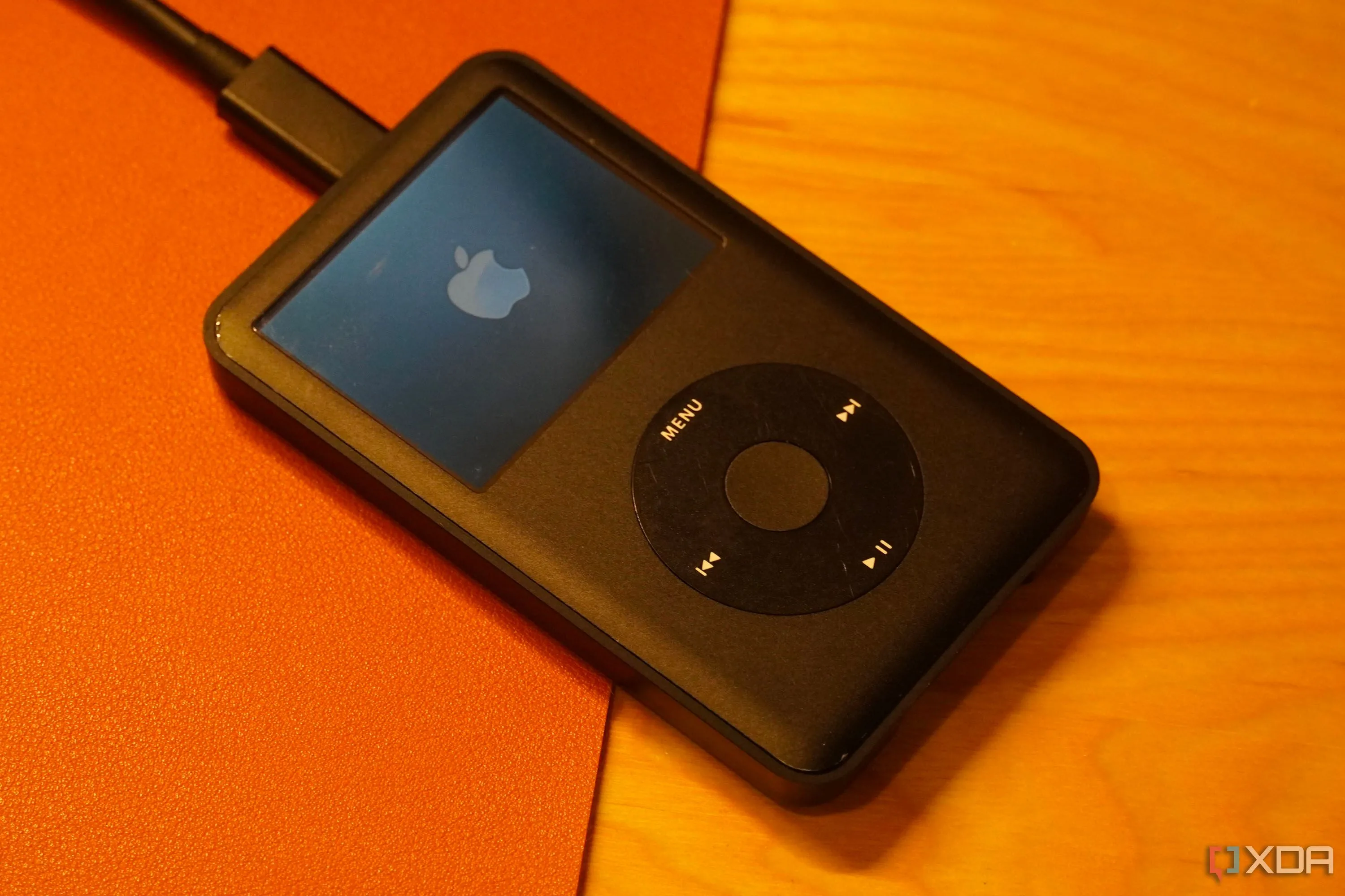 iPod Classic màu trắng với bánh xe điều khiển click wheel và logo Apple, biểu tượng của kỷ nguyên máy nghe nhạc di động.