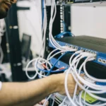 Kỹ sư mạng đang cắm cáp Ethernet vào thiết bị switch, tượng trưng cho việc quản lý và cập nhật bảo mật hệ thống