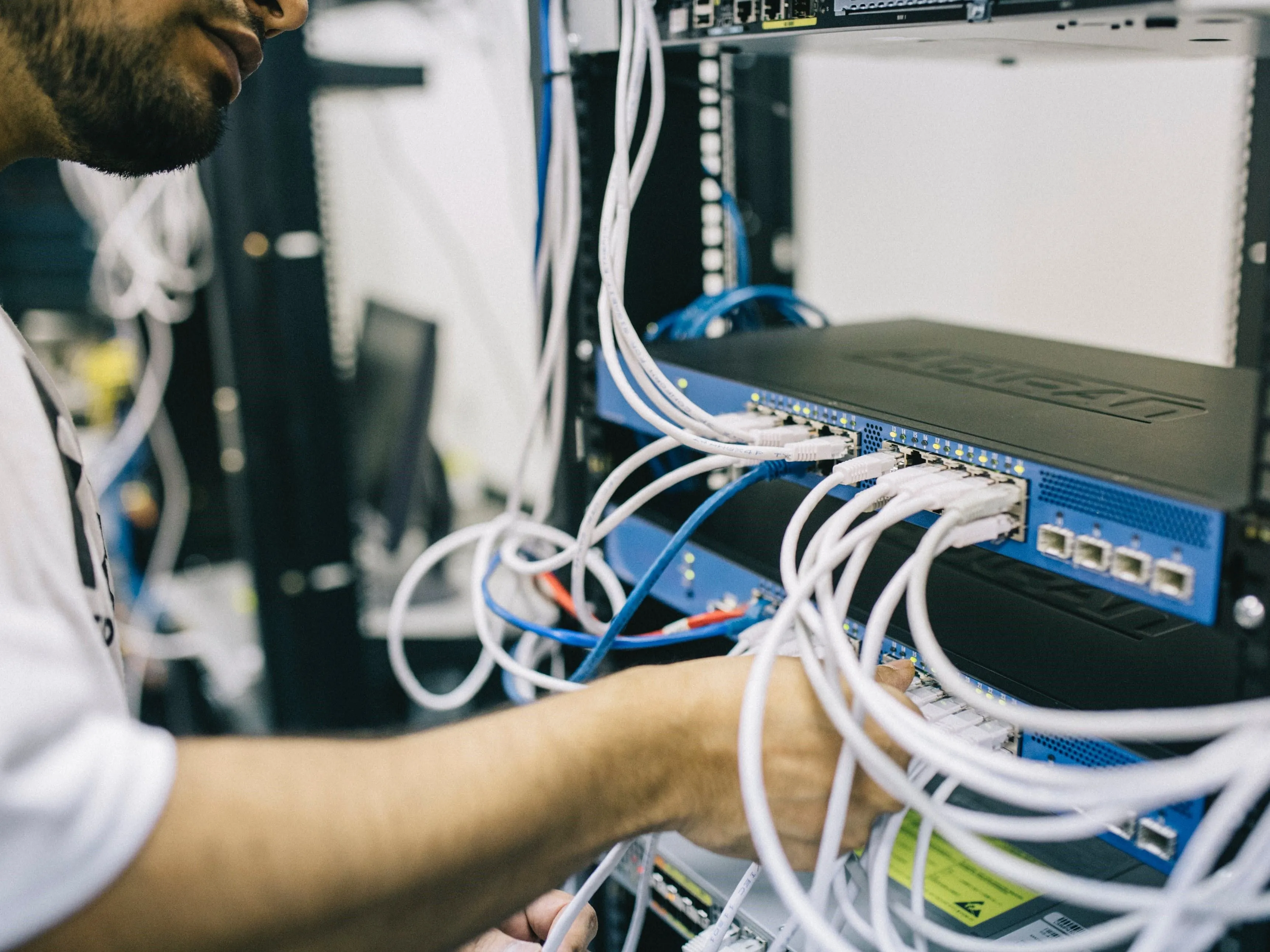 Kỹ sư mạng đang cắm cáp Ethernet vào thiết bị switch, tượng trưng cho việc quản lý và cập nhật bảo mật hệ thống