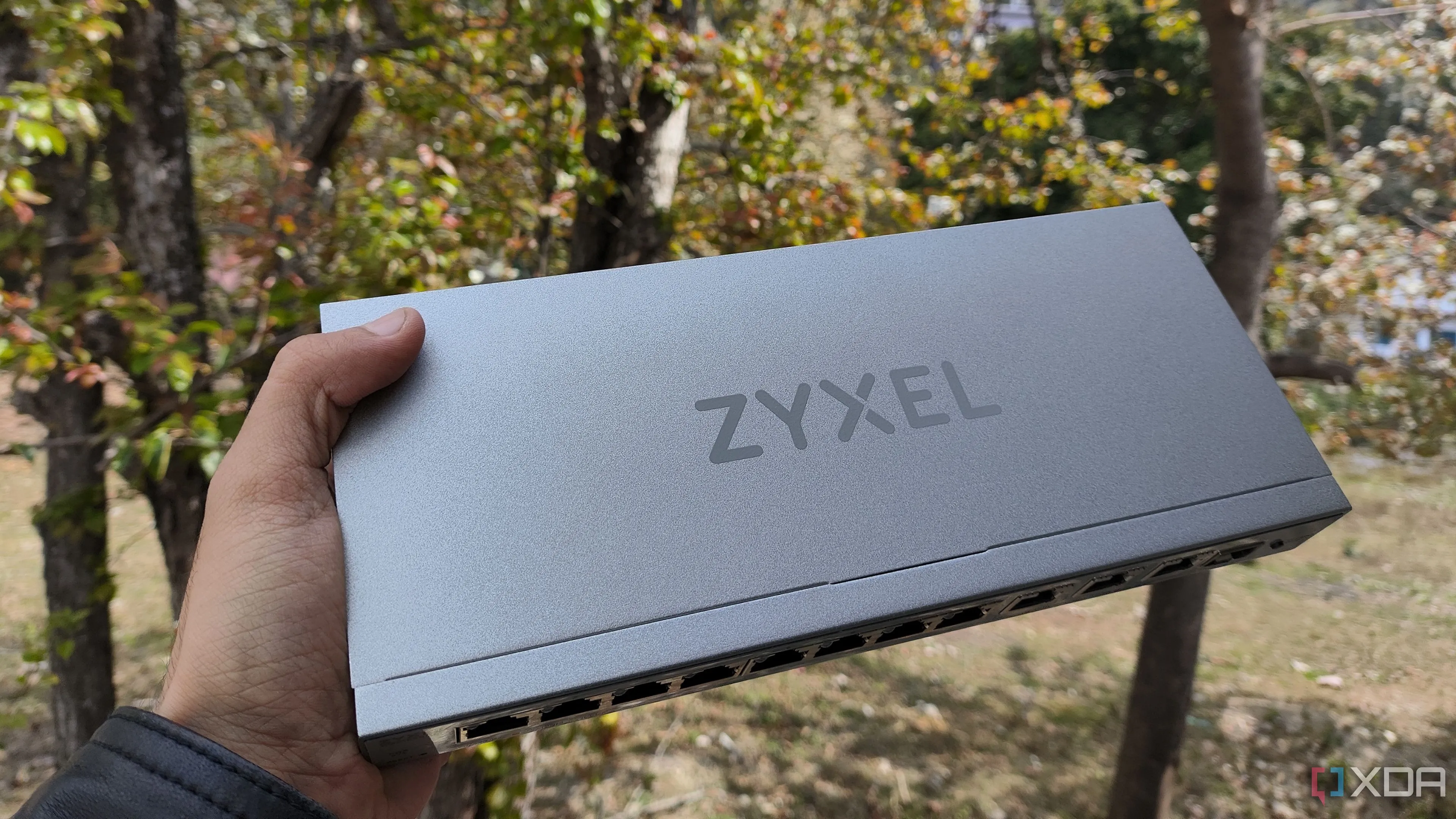Một người đang cầm switch mạng Zyxel, đại diện cho thiết bị mạng giúp giảm nhiễu và mở rộng khoảng cách