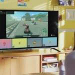 Một người phụ nữ đang ngồi nhìn màn hình TV hiển thị game Nintendo Switch 2 với giao diện GameChat