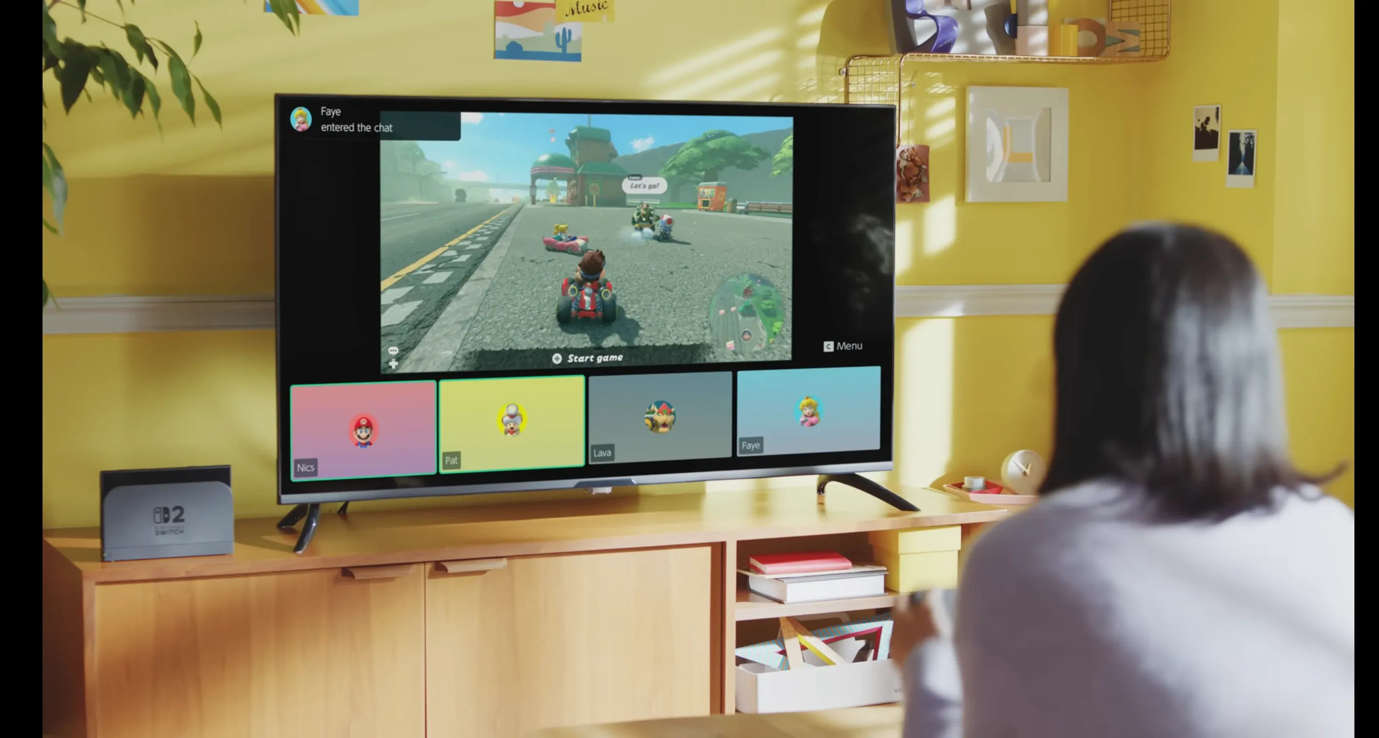 Một người phụ nữ đang ngồi nhìn màn hình TV hiển thị game Nintendo Switch 2 với giao diện GameChat