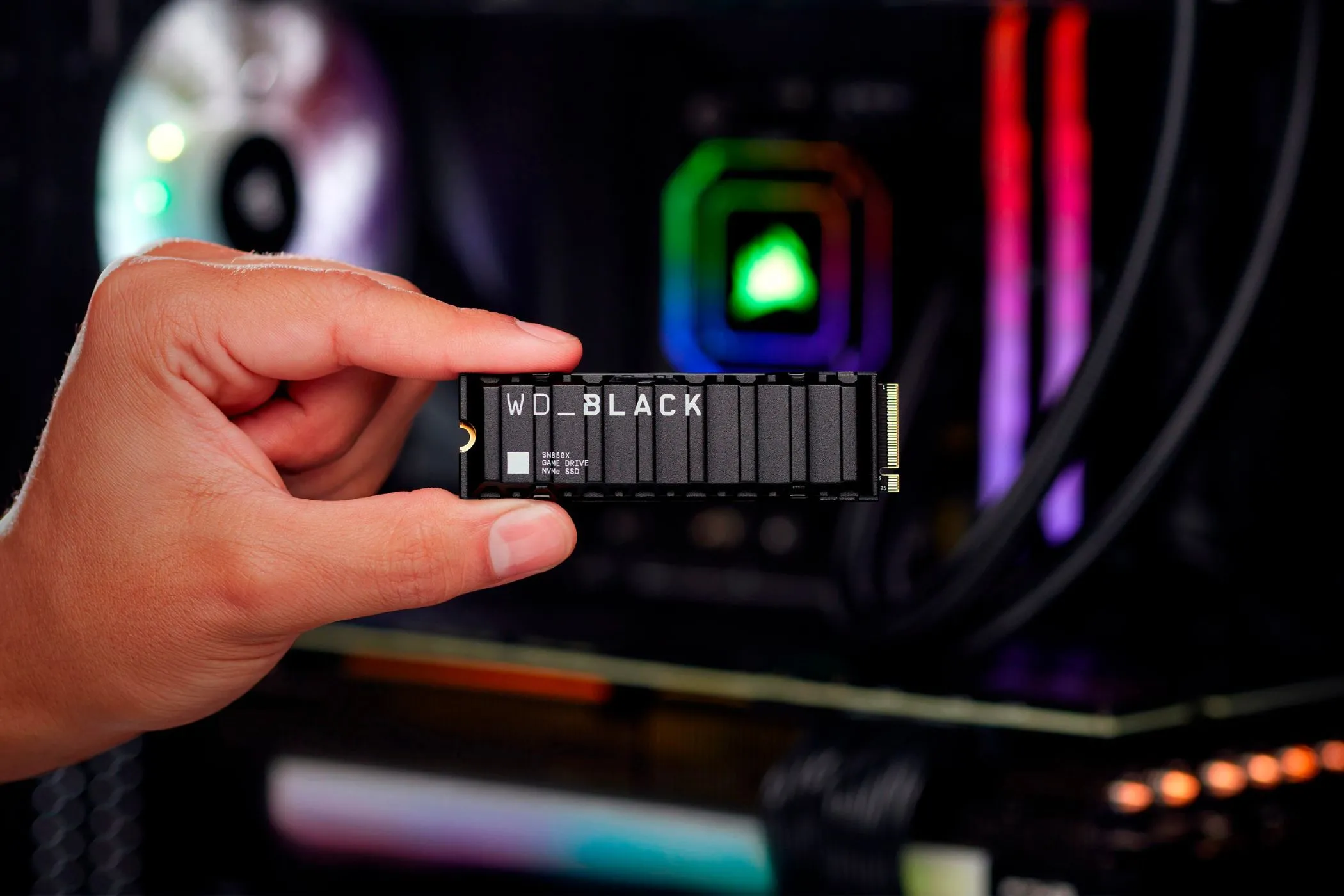 Người dùng cầm ổ cứng SSD WD Black SN850X Gaming cùng dàn máy tính PC chơi game có đèn RGB phía sau