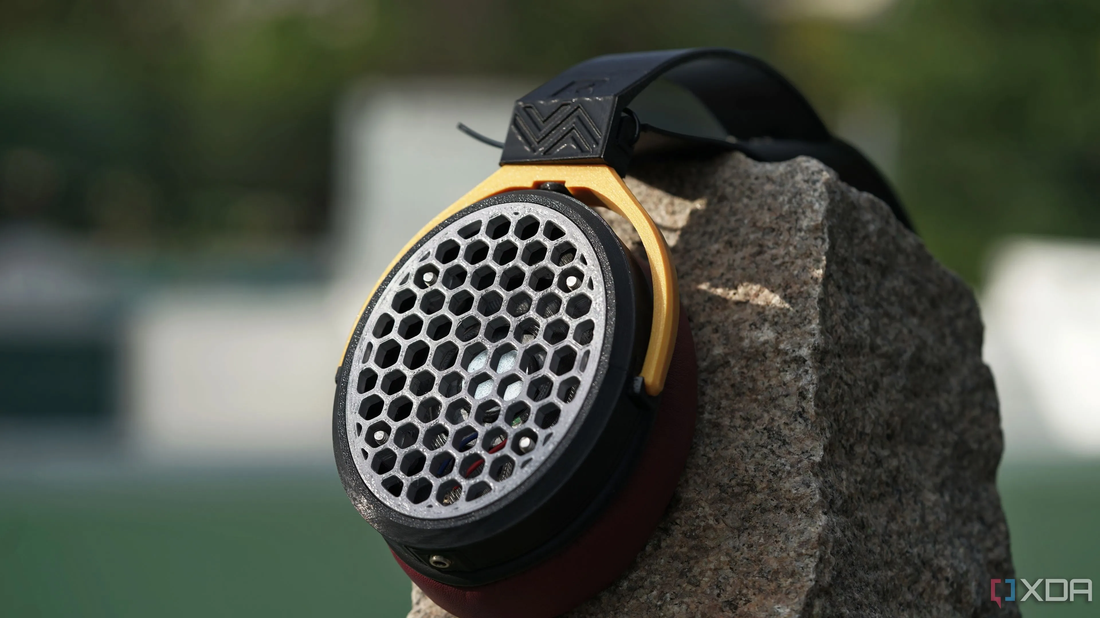 Tai nghe in 3D dạng mở đặt trên một tảng đá với chỉ một earcup hiển thị trên nền mờ